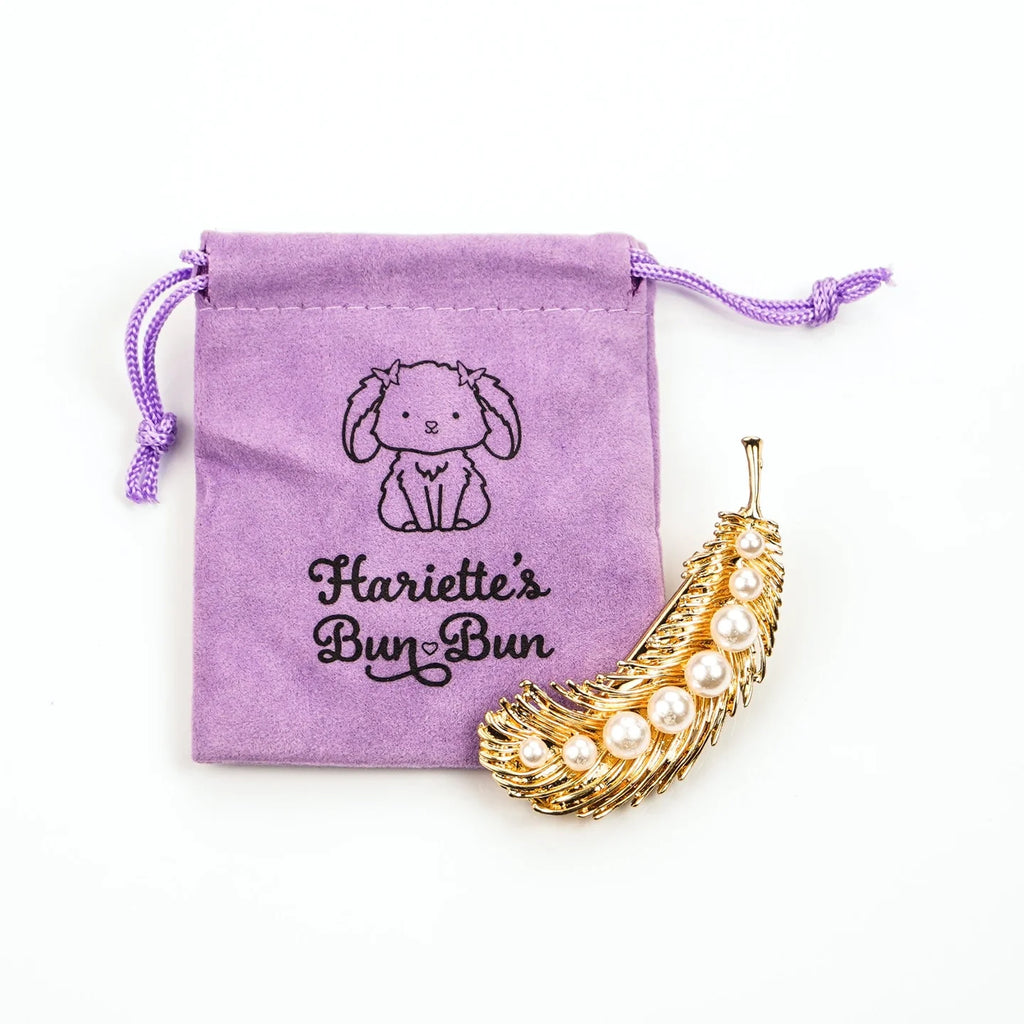 A leaf design gold and pearl hair accessory next to a storage bag